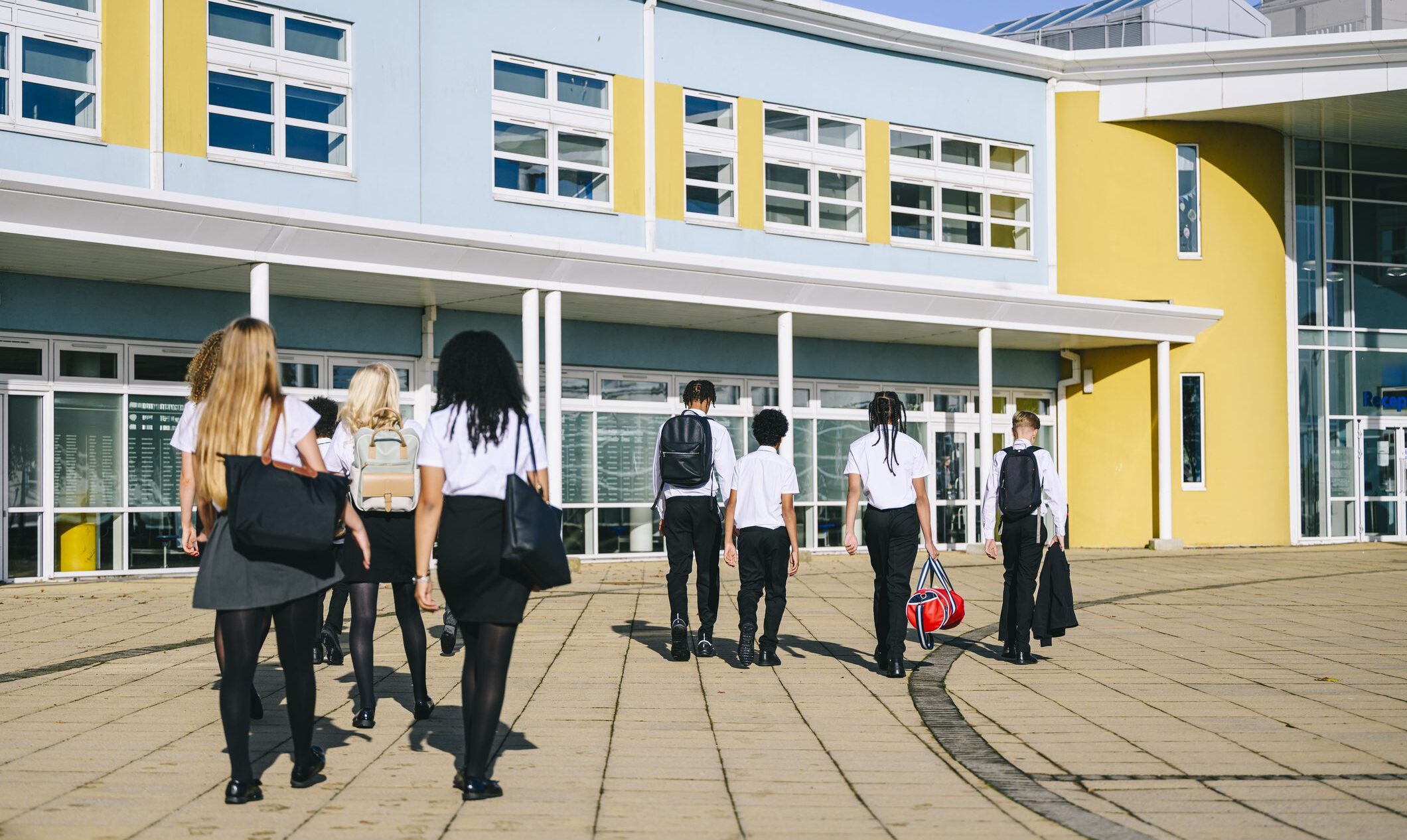 High school students wearing uniform walking to school entrance carrying bags